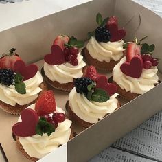 a box filled with cupcakes covered in frosting and topped with fresh fruit