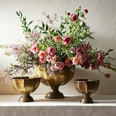 three brass vases with flowers in them on a ledge next to a white wall