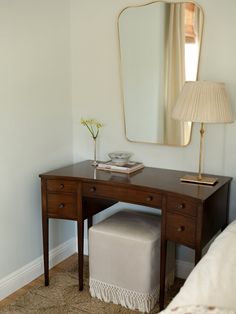 a desk with a mirror, stool and lamp in a room