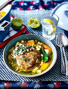 a bowl filled with meat and vegetables on top of a blue table cloth next to silverware