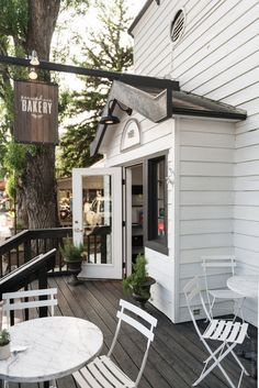 an outdoor patio with white chairs and a small table on the deck next to a tree