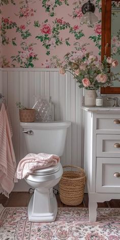 a white toilet sitting next to a sink in a bathroom under a mirror with pink flowers on it