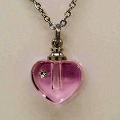 "A sparkle of clear CZ makes this art glass cremation urn necklace even more striking than the original. Our gorgeous CZ accented art glass heart urns are all made by hand by skilled artisans, each is a work of art, and no two are exactly alike. Our glass hearts come in three beautiful colors - a petal pink, medium lilac or a beautiful blue. Inside the screw topped CZ accented glass heart urn there's a small chamber to hold human or pet cremation ashes, beach sand, Sacred Earth, or dried ceremon Clear Glass Keepsake Necklaces, Clear Glass Necklaces For Keepsake, Clear Glass Keepsake Necklace, Clear Glass Keepsake Jewelry, Glass Keepsake Jewelry In Clear, Sacred Earth, Glass Hearts, Pet Cremation, Urn Jewelry