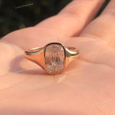 a close up of a person's hand holding a ring with an oval shaped diamond