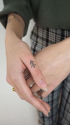 a woman's hand with a tiny arrow tattoo on it