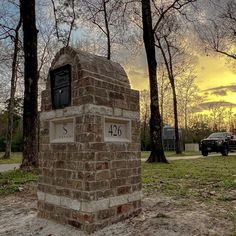 a brick monument in the middle of a grassy area with trees and a police car behind it