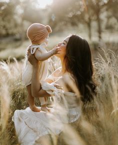 a woman holding a baby in her arms while sitting on the ground with tall grass