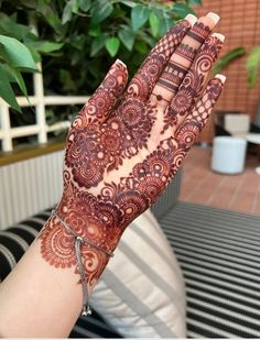 a woman's hand with henna tattoos on it, and a plant in the background