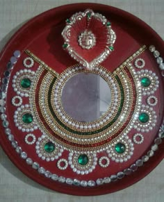 a red plate with some green and white jewels on the top, and a mirror in the middle