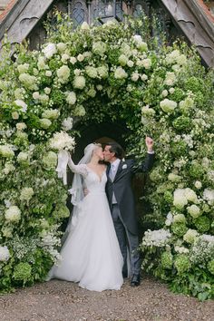 a bride and groom kissing in front of a floral arch