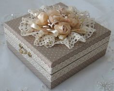 a decorative box with lace and flowers on it sitting on a white cloth covered tablecloth