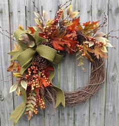 a wreath with leaves and berries hanging on the side of a wooden fence in autumn