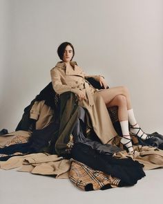 a woman sitting on top of a pile of clothes wearing high heeled shoes and trench coat