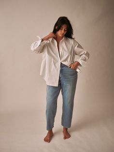 a woman is standing in front of a gray background wearing jeans and a white shirt