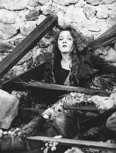 black and white photograph of a woman with long hair sitting on the ground in front of a stone wall