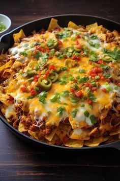 a skillet filled with nachos, cheese and green onions on a wooden table