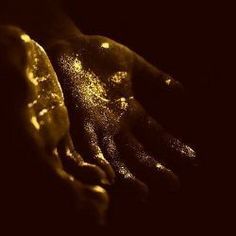 two hands are covered in yellow powder on a black background with the light shining through them