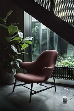 a red chair sitting in front of a window next to a plant on the floor