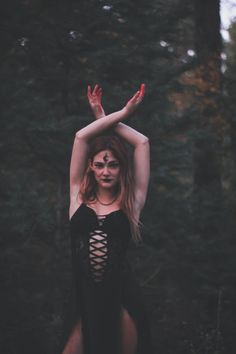 a woman with red makeup is standing in the woods holding her hands above her head