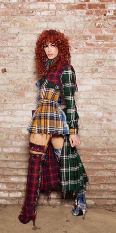 a woman with red hair is standing in front of a brick wall wearing plaid clothes