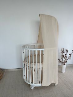 a white crib next to a wall with a curtain on it and a potted plant in the corner