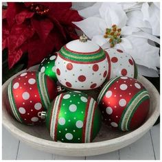 a bowl filled with red and green decorated christmas ornaments next to a white poinsetti