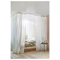 a bed sitting under a window next to a white curtained wall and wooden floor