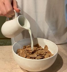 a person pouring milk into a bowl of cereal