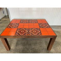 an orange and brown tiled table with flowers on the top, in front of a white wall