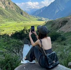 a woman sitting on top of a rock holding a cell phone up to her face