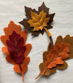 three felt autumn leaves laying on top of a white table cloth covered in brown, orange and red colors