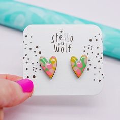 a pair of pink and green heart shaped earrings on top of a card with the words stella and wolf