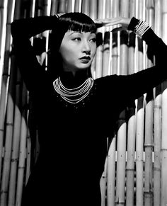 black and white photograph of a woman in front of bamboo wall with her hands on her head