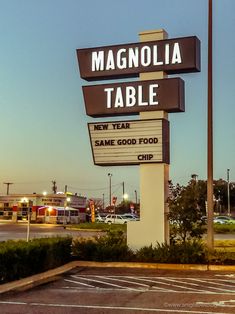 a sign for a restaurant called magnolia table with cars parked in the lot behind it