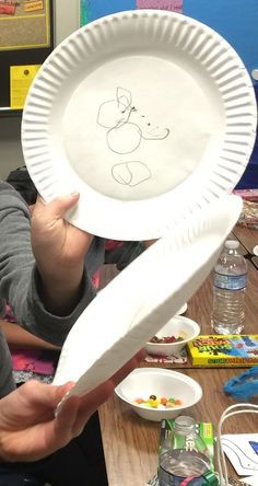 a young boy holding up a paper plate with a drawing on it's side