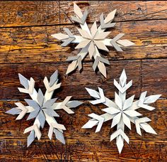 three paper snowflakes are sitting on a wooden surface, one is white and the other is silver