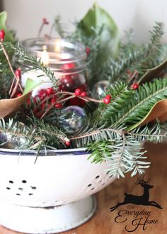 a bowl filled with candles and greenery on top of a wooden table next to a candle