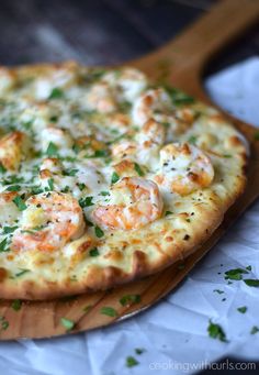 a pizza with shrimp on it sitting on top of a wooden cutting board