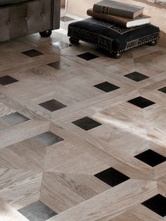 a living room with black and white tile flooring next to a chair, ottoman and coffee table