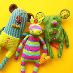 three crocheted stuffed animals laying next to each other on a yellow surface,