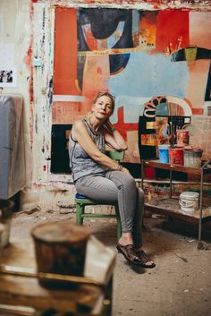 a woman sitting on a chair in front of a wall with art work behind her