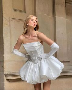 a woman in a short white dress posing for the camera with her hands on her hips