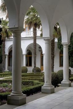 an outdoor courtyard with many trees and bushes in the foreground, surrounded by white pillars