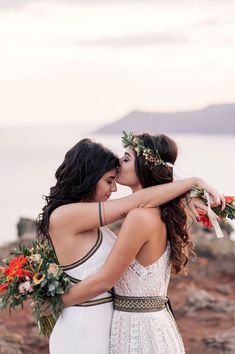 two women in white dresses hugging each other with flowers around their necks and one woman wearing a flower crown