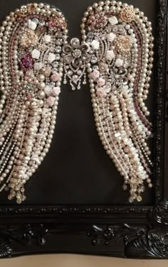 two angel wings made out of pearls and other beads in a black frame on a table