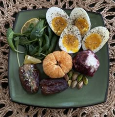 a green plate topped with eggs, fruits and vegetables on top of a woven table cloth