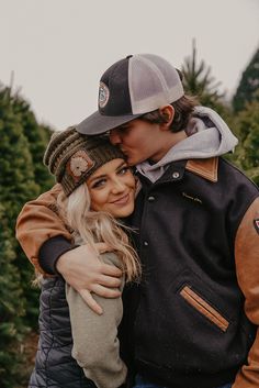 a young man and woman hugging each other in front of a christmas tree farm filled with trees