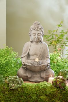 a buddha statue sitting on top of a lush green field next to a lit candle