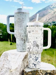 two travel mugs sitting on top of a rock