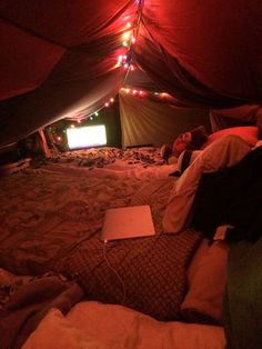 there is a laptop on the bed in this tent with lights strung from it's ceiling